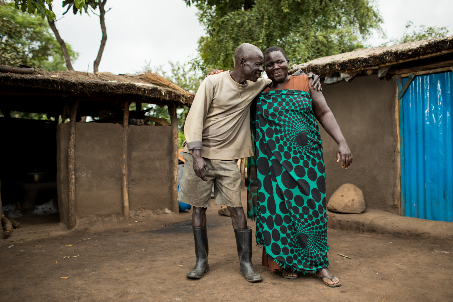 SE savings group member, Flora with her husband Benson in front of their home in the refugee settlement. Photo by Esther Havens.